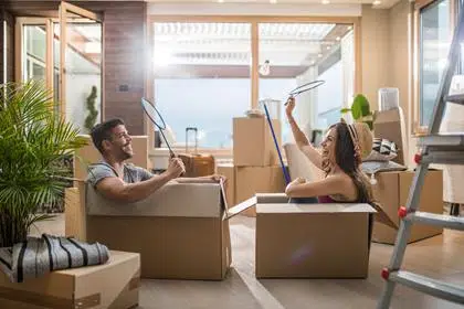 Joven pareja feliz sentada en cajas de cartón en su nuevo hogar y divirtiéndose mientras juegan al bádminton.